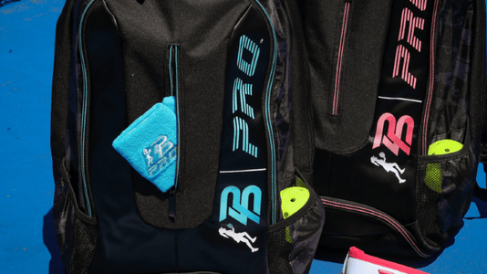 Black PBPRO Tour backpacks with seafoam and pink accents beside matching visors