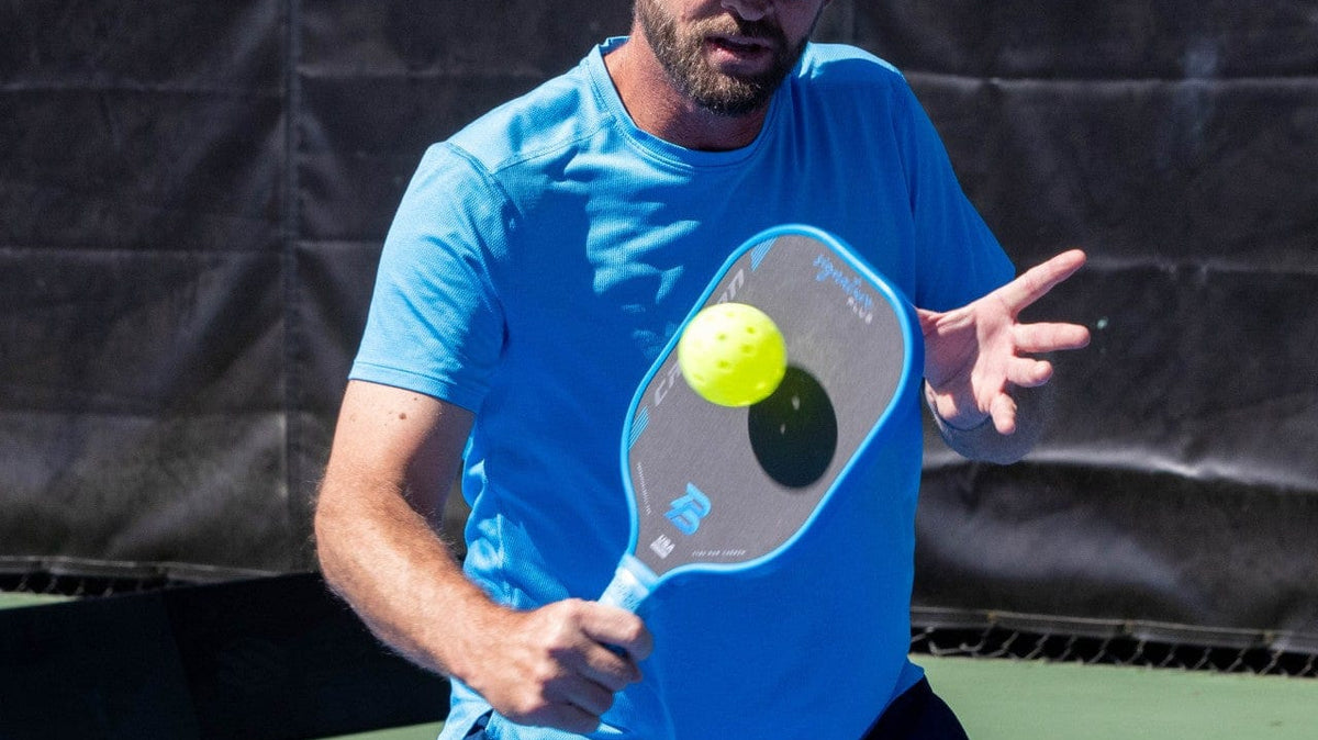 Blue PB Signature Plus 16mm T700 pickleball paddle, used by a player hitting a ball