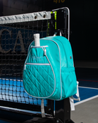 Mint PBPRO Signature pickleball backpack, hanging from a court net with a paddle