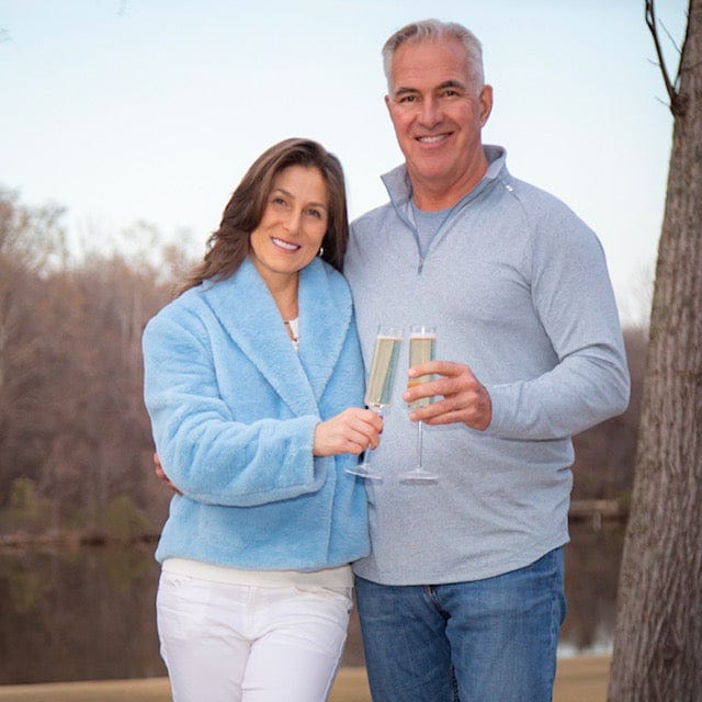 Man and woman holding champagne glasses outdoors with a lake in the background